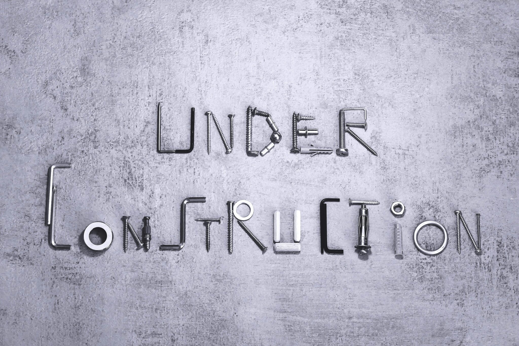 Under construction text creatively formed using various screws and tools on a concrete background.